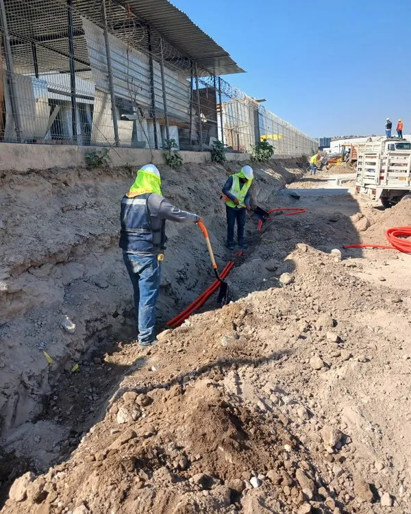 Dos técnicos tendiendo ducto eléctrico rojo en una zanja abierta en obra