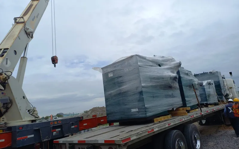 Grúa realizando maniobra de descarga de equipo pesado sobre plataforma en obra
