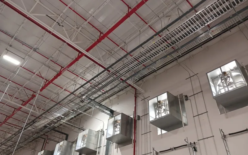 Charolas de cableado y luminarias industriales montadas bajo la estructura de la nave